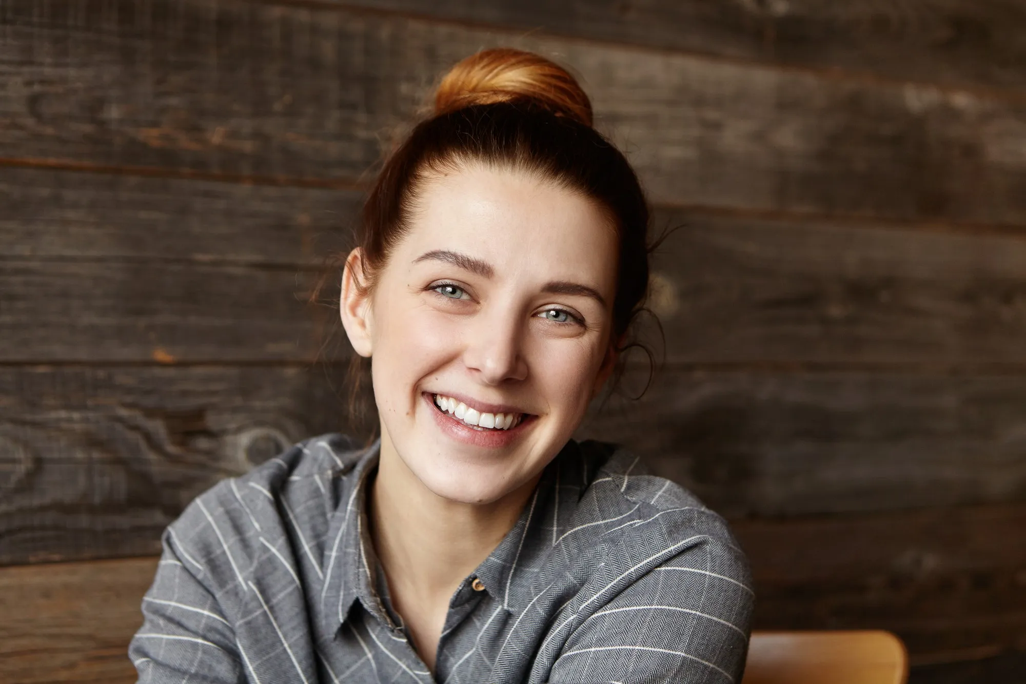 Mujer joven sonriendo con expresión alegre frente a una pared de madera