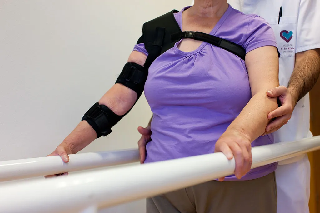 un profesional de fundacion hospitalarias ayuda a una mujer a caminar en unas barras