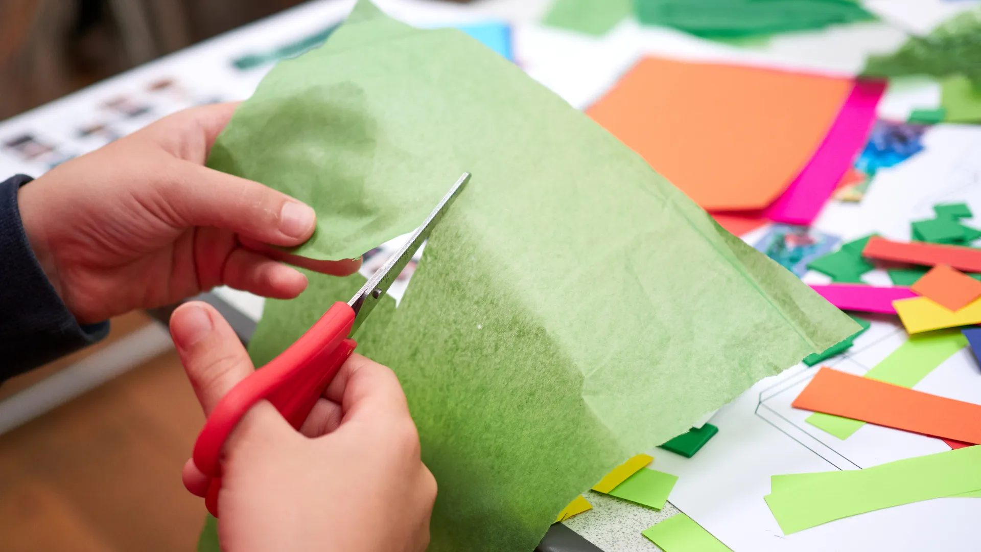 manos con tijeras recortando papel de colores