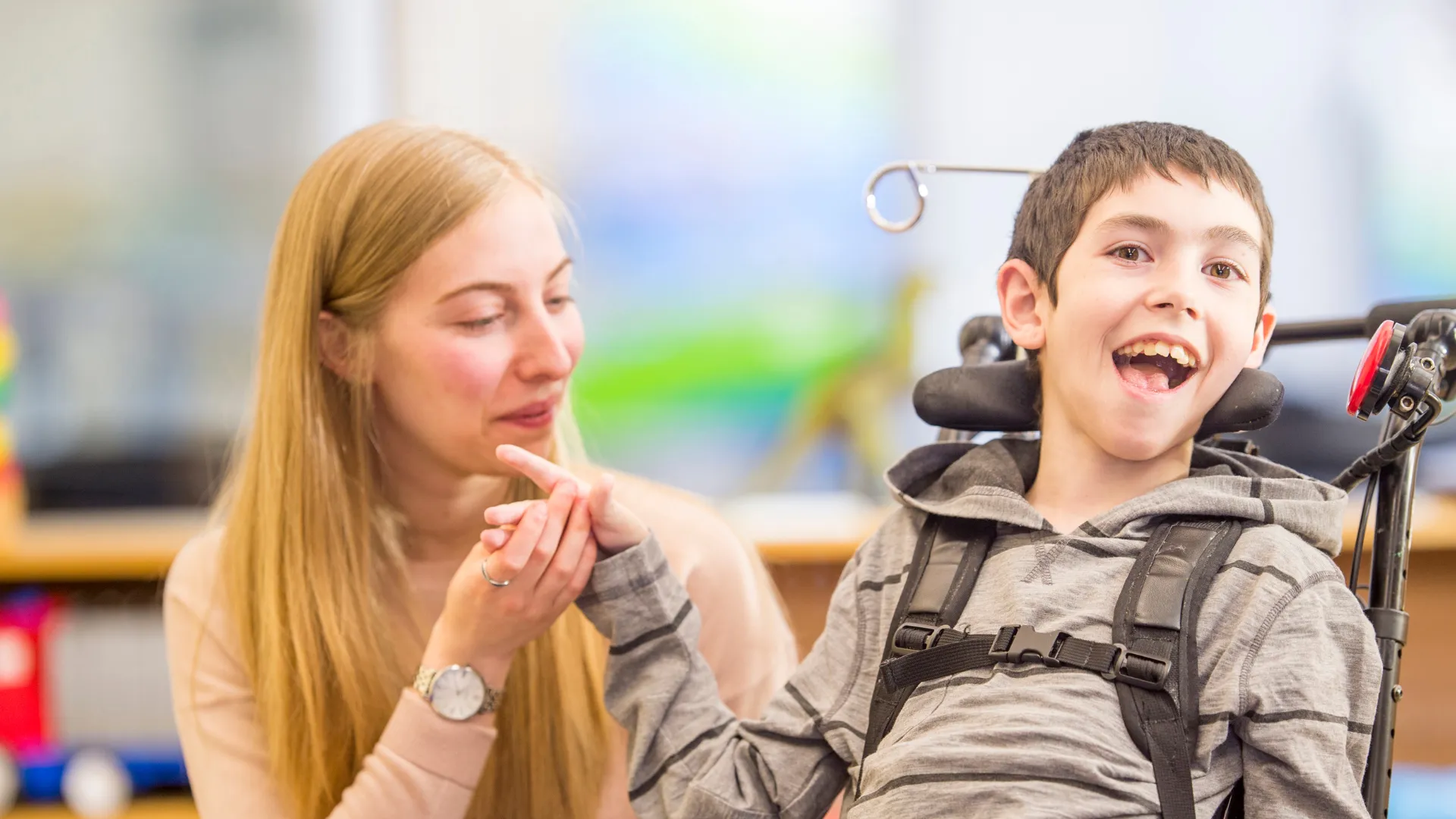 Persona adulta sostiene la mano de un niño que está sentado en una silla de ruedas con soporte para la cabeza
