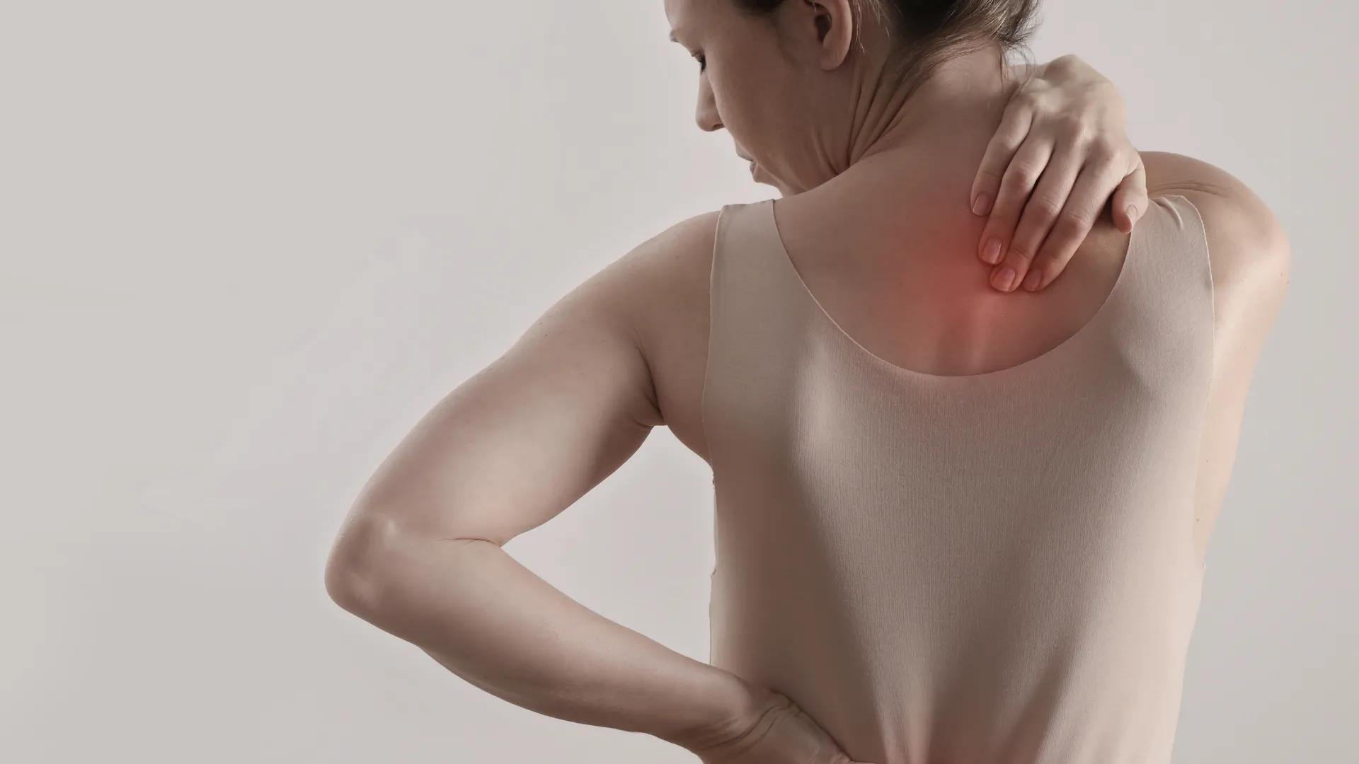 Persona vista de espaldas con camiseta sin mangas, tocando la zona superior de la espalda y el cuello con una mano y la parte baja de la espalda con la otra