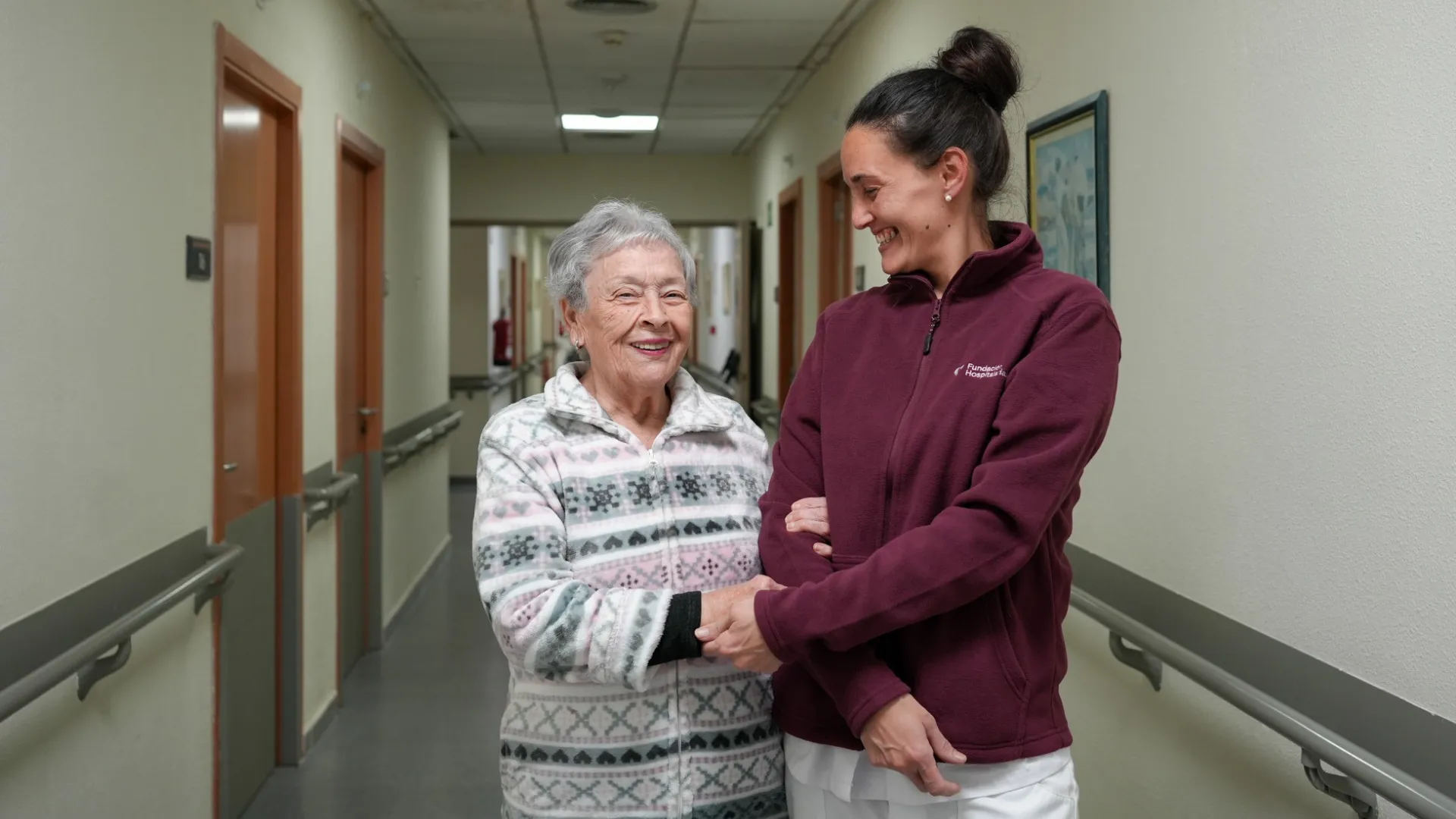 trabajadora de Fundación Hospitalarias con una mujer mayor en un pasillo