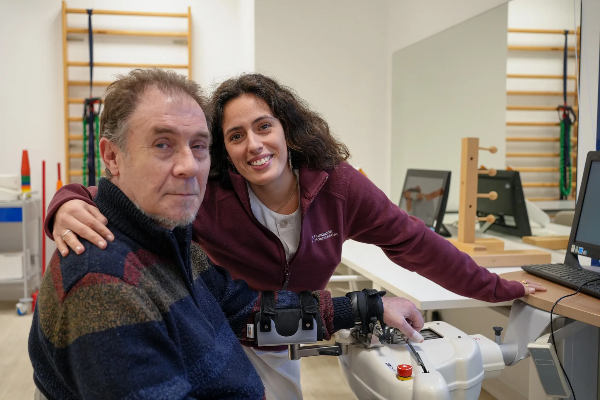 profesional de Ospitalarioak Fundazioa Euskadi junto a un usuario de un brazo robótico