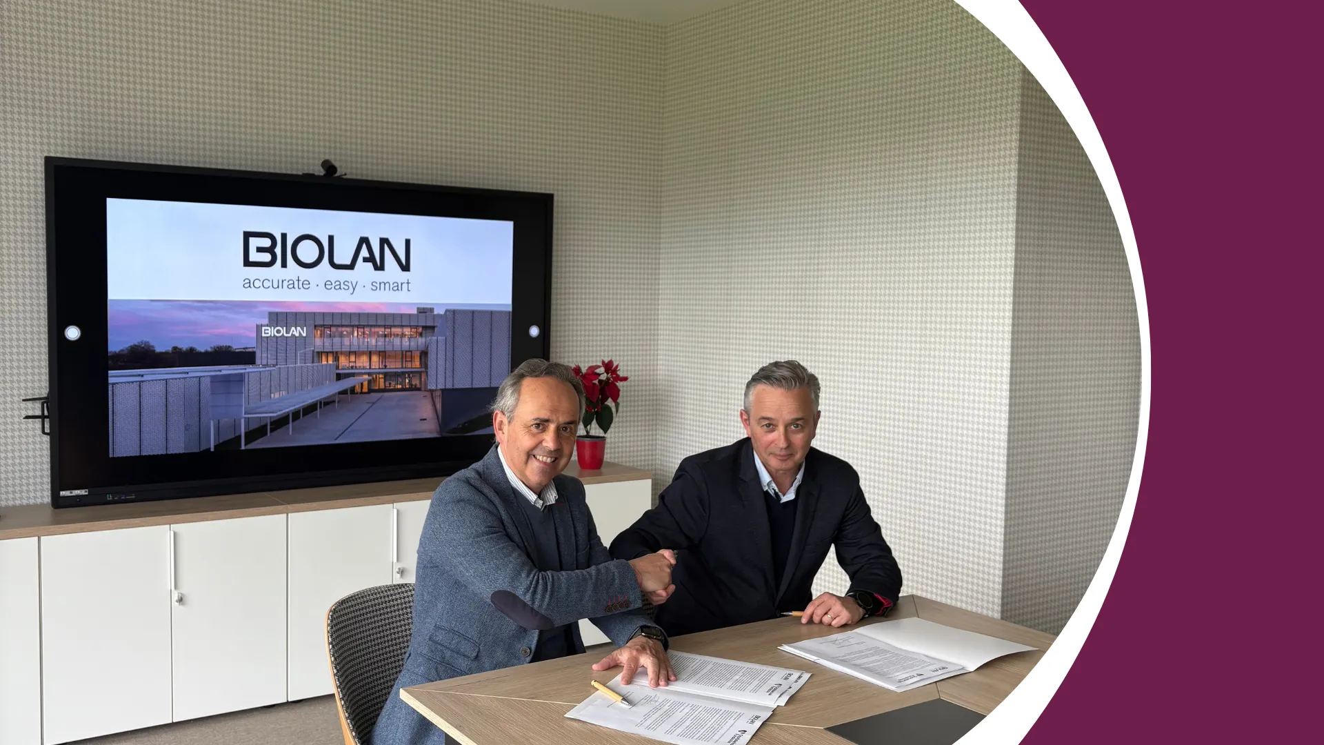 Dos hombres estrechan la mano mientras firman un acuerdo en una sala de reuniones. En el fondo, una pantalla muestra el logotipo de Biolan con el lema “accurate · easy · smart” y una imagen del edificio de la empresa.