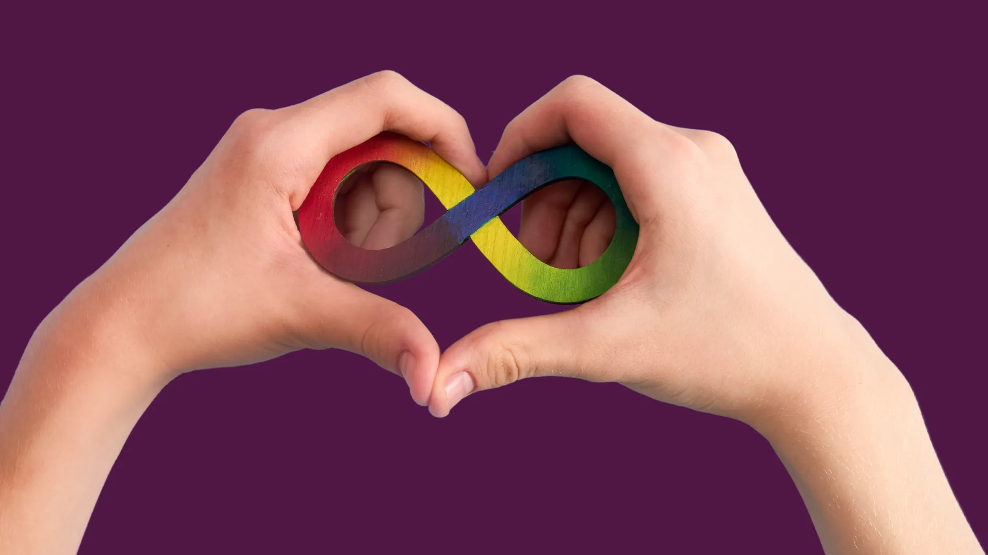 Dos manos forman un corazón alrededor del símbolo del infinito con los colores del espectro autista (rojo, amarillo, verde, azul y púrpura), sobre un fondo morado.